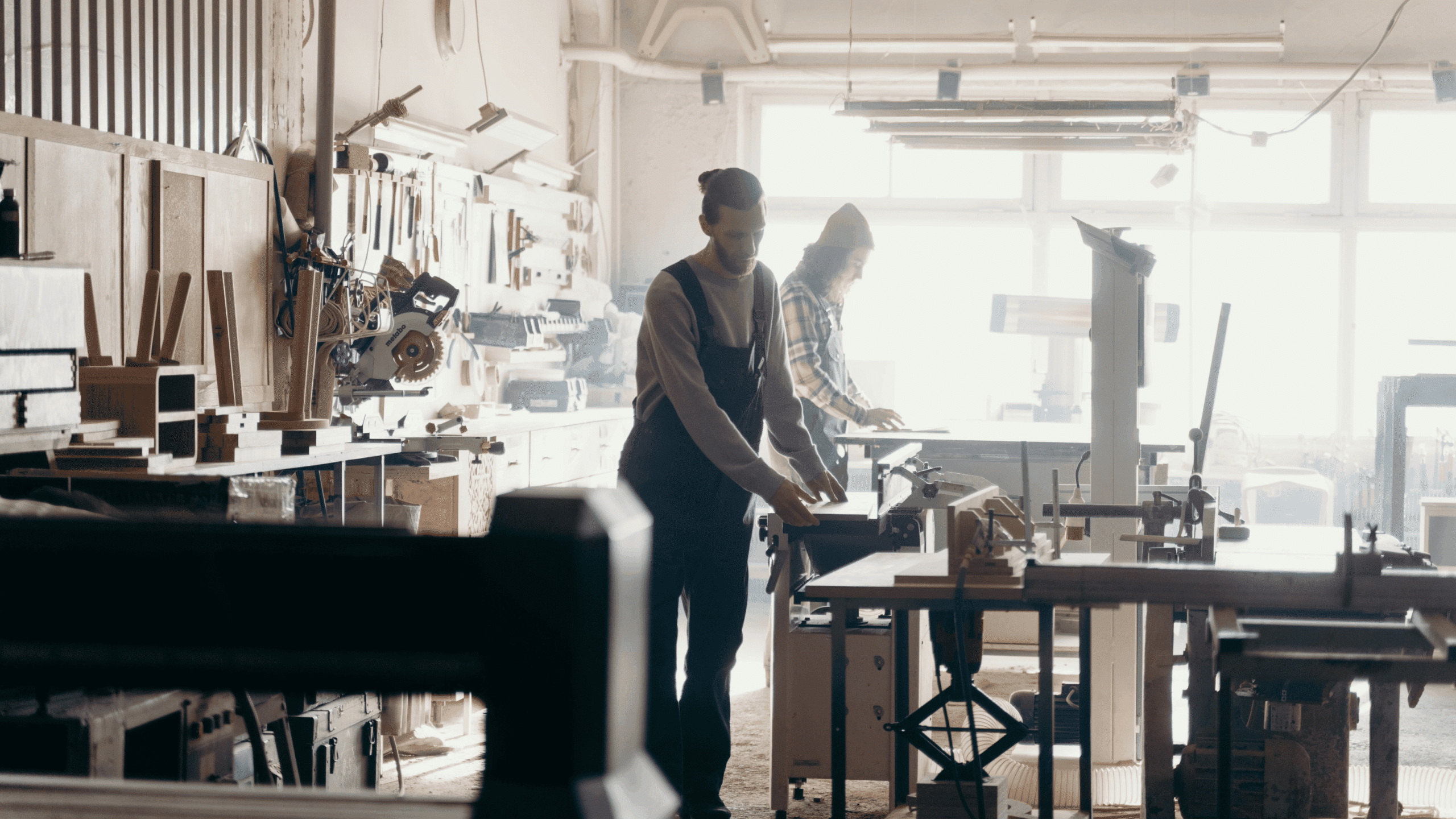 Deux artisans travaillant le bois dans un atelier équipé de machines et outils de menuiserie